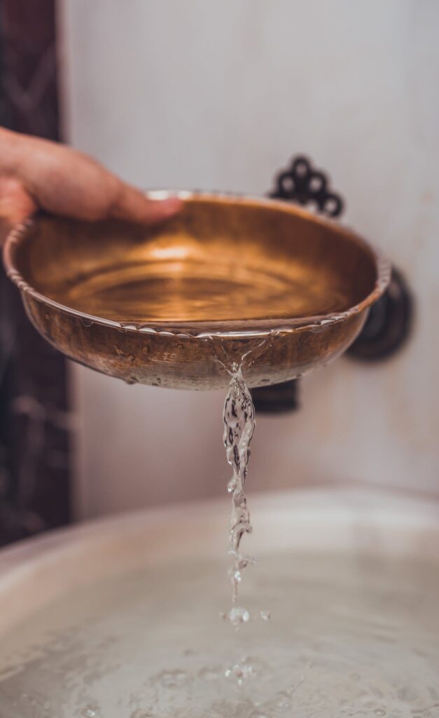 A person holding a metal bowl over a sink